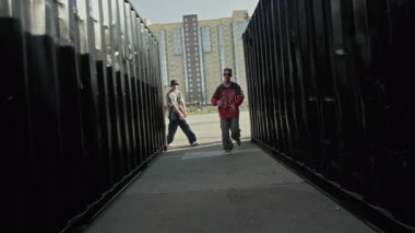 Kenar mahallelerde, arka planda bulanık bir apartman bloğuyla kameraya bakarken şık hip hop kıyafetleri içinde dört kendinden emin Z-boy 'un el kamerasıyla çekilmiş görüntüsü.