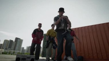 Kafkas jenerasyonu Z B-boy 'un arka planda akranlarının önünde break dans hareketleri yaparken, açık havada açık hava müziği eşliğinde parlak güneşli bir günde