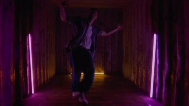 Şehir kıyafetleri içindeki genç yaratıcı beyaz çocuk mor ışık altında kapalı alanda dans ederken rock 'n' roll 'un rock' n 'roll hareketlerini icra ediyor.