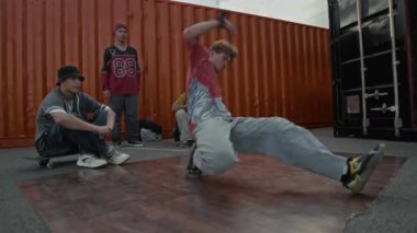 Sokak kıyafetleri içindeki yetenekli beyaz çocuk dışarıda müzik eşliğinde doğaçlama yaparken ve arkadaşlarının önünde rock hareketleri yaparken el kamerasıyla çekilmiş.