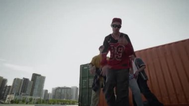 Yetenekli, beyaz bir gencin açık havada dans edip mükemmel ayak hareketlerini ve yaratıcılığını sergilediği, parlak bir yaz gününde akranlarıyla birlikte doğaçlama müzik yaptığı el kamerasıyla çekilmiş bir fotoğraf.