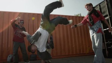 Kentsel giyim içindeki yetenekli beyaz Z B-Boy 'un yavaş çekimleri akranlarının önünde nefes kesici amuda kalkıyor. Güneşli bir günde onu izliyor ve destekliyor. Açık havada break dans yapıyor.