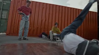 Yetenekli beyaz break dansın muhteşem omuz hareketini yaparken bacaklarını havaya kaldırarak vücudunu döndüren genç arkadaşlarıyla dışarıda pratik yaparken elde çekilmiş bir fotoğraf.