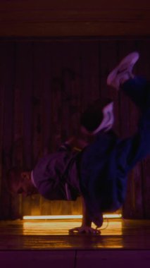 Dikey yavaş çekimde sokak elbiseli beyaz çocuk vücudunu döndürürken kucağında zıplayarak neon ışığın altında çağdaş break dans yapıyor.