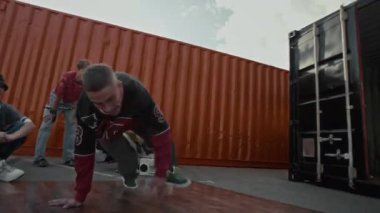 Kenar mahalleli kendinden emin beyaz çocuk B-boy 'un nefes kesici break dans hareketleri yaparken vücudunu döndürüp dışarıda onu izleyenler arasında pratik yaparken elde çekilmiş bir fotoğrafı.