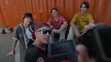 Sokak tarzı giyinmiş genç beyaz bir çocuğun POV 'u VHS kamerayla video bloğu kaydederken konuşuyor yerde oturuyor ve dışarıdaki kameralara poz veren arkadaşlarıyla takılıyor.