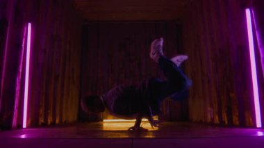 Güçlü beyaz çocuğun zemin seviyesinde yavaş çekim. Elinde dönen, renkli ortam ışıkları altında nefes kesici break dans hareketleri yapıyor.