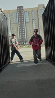 Kenar mahallelerde, arka planda bulanık bir apartman bloğuyla kameraya bakarken şık hip hop kıyafetleri içinde dört kendine güvenen beyaz B-boy dikey el kamerası görüntüsü.