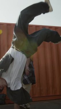 Kentsel giyim içindeki yetenekli beyaz Z-B-boy dikey yavaşlama. Akranlarının önünde nefes kesici amuda kalkıyor. Güneşli bir günde onu izliyor ve destekliyor.