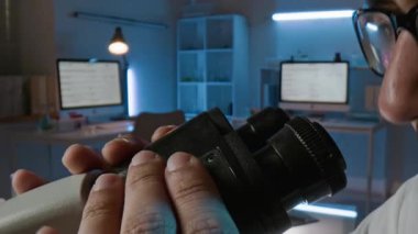 Tıp laboratuarında çalışırken gözlük takan erkek bilim adamının mikroskop üzerindeki mercekleri ayarlarken yakın plan fotoğrafı.