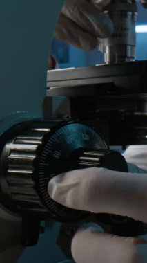 Laboratuvar ortamında deney yaparken koruyucu eldivenli, mikroskobu dikkatlice kullanan tanınmayan araştırmacıya dikey yakın çekim