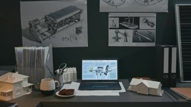 Yenilenebilir enerji ofisindeki maketlerin, belgelerin ve teknik çizimlerin yakınındaki dizüstü bilgisayarlı monitörde yatay eksen pervaneli 3D dijital rüzgar türbini modeli çekilen kimse yok.