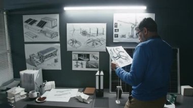 Güneş panelleri ve rüzgar türbinlerinin planlarına bakan ve sürdürülebilir teknoloji ofisindeki yel değirmeni pervanelerini gösteren planlar geliştiren kıdemli yenilenebilir enerji mühendisinin arka görüntüsü