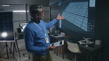 Yetişkin Hintli erkek temiz enerji mühendisinin tablet bilgisayarlı orta boy fotoğrafı. Ofisteki bilimsel toplantıda multimedya ekranında yeni dijital güneş enerjisi sistemi modelini gösteriyor.