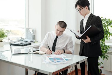 Takım elbiseli genç Asyalı patronunun kağıtları imzalamasını bekliyor.