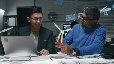 Asyalı ve Hintli müteahhitlerin küçük bir maket kullanarak rüzgar türbininin çalışmalarını inceleyip yenilenebilir enerji ofisinde yeni bir model tasarladıkları orta boy bir fotoğraf.