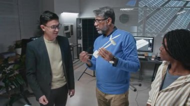 Yetişkin Hintli erkek mühendisin çeşitli stajyerlere küçük model kullanarak sürdürülebilir teknolojiler geliştirerek rüzgar türbininin yapısını ve çalışmalarını açıklarken orta uzunlukta bir çekim.