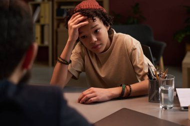 Üzgün okul çocuğu sorunlarını tartışırken kafasına dokunuyor ve olgun okul psikoloğuna bakıyor.