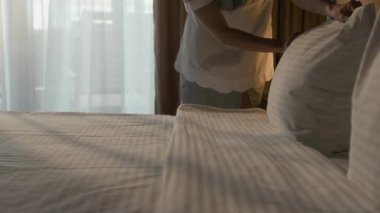 Otel odasında yatağı düzeltirken, çarşafları düzelten ve yastıkları ayarlayan hizmetçiyi yakın çekim.