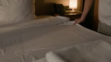 Kadın hizmetçinin ellerini kapat. Yatağın üzerinde yumuşakça beyaz çarşaflar seriyor. Ilık bir şekilde aydınlatılıyor.