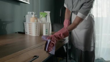 Ev sahibesinin üniformalı, koruyucu eldivenli, ahşap masayı kumaşla silerken otel odasını temizleyen misafirler için görüntüsünü kapatın.