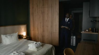 Formalite icabı otel yöneticisi dijital tablet tutuyor ve ziyaretçilere sunum odası sunuyor, konfor ve uzay düzenlemelerini açıklıyor