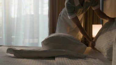 Otel temizlikçisinin yastıkları kabartması ve misafir odasının penceresinin yanındaki beyaz çarşafları düzleştirmesi.
