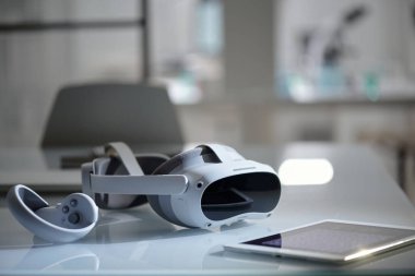 Çağdaş ofisteki yansıtıcı masada parlak sanal gerçeklik kulaklığının yakın çekimi. Sahne aksesuar ve tablet içeriyor, ileri teknoloji ile karıştırılmış yüksek teknoloji ortamı öneriliyor