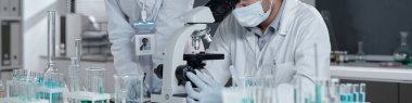 Laboratuvar ortamında mikroskop ve camla çalışan laboratuvar önlüğü ve maskeleri giyen araştırmacılar, bilimsel araştırma ve analizlere odaklanıyorlar.