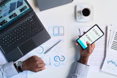 Ofisteki iş yerinde online hesap makinesi uygulaması kullanan tanınmayan erkek elleri yukarıdan görülüyor.