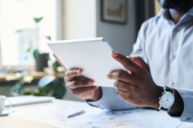 Dijital tablet tutan tanınmayan siyahi adamın elleri, ofiste sunum yapmak için kullanılıyor.