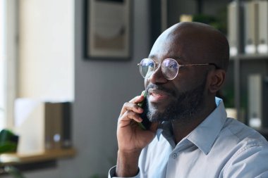 Gözlüklü neşeli genç Afrikalı Amerikalı iş ortağıyla telefonda konuşuyor.