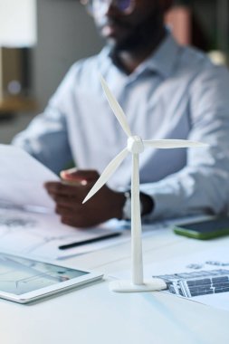 Ofis masasında oturan Afrikalı Amerikalı mühendise ait plastik rüzgar türbini modelinin dikey yakın çekimi.