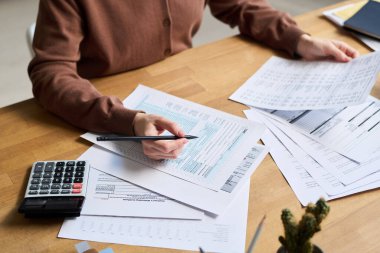 Masasında oturan, elinde kalemle banka belgelerinin kağıt kopyalarını inceleyen tanınmayan genç bir kadının yüksek açılı yakın çekimi.