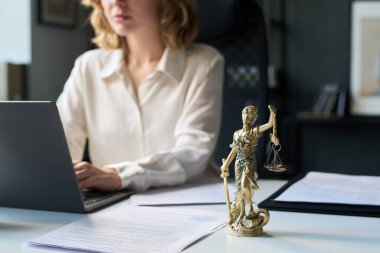 Ofiste yalnız çalışan kadın avukat, masada dizüstü bilgisayar kullanarak, Adalet Anıtı 'nın bronz heykelciğine odaklan.