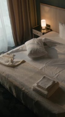 Kadın temizlikçinin, temiz havlu getirdiği ve rahat bir otel odasında yatak yaptığı dik açılı bir fotoğraf.