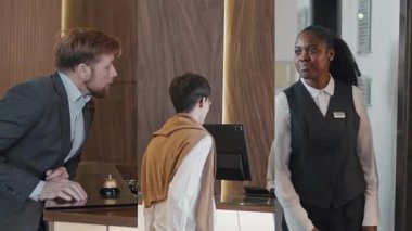 Erkek turistlerin ve iş adamlarının otel resepsiyonuna giriş yaparken ve asansöre girerken ekran görüntülerini böl, kadın işçi misafirlere yardım ediyor