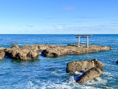 Ooarai Isosaki Tapınağı 'ndan Torii, kayanın tepesinde küçük bir tapınağı olan kayalık bir kıyı şeridi. Su sakin ve gökyüzü berrak.
