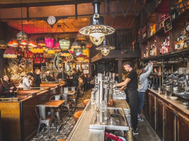 Fransa, Paris, 17 Kasım 2024, Cafe Charbon, iki barmen renkli lambalı kalabalık bir klasik barın arkasında içki hazırlıyor.