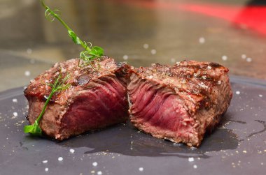 Siyah arka planda baharatlı ızgara biftek. Biberiye ve deniz tuzu serpilmiş çatallı biftek.