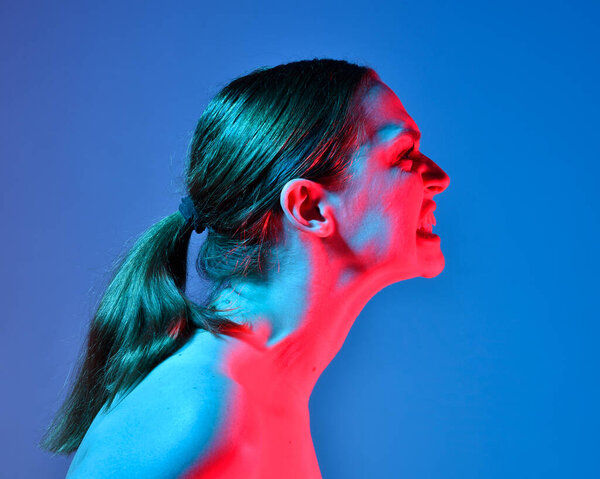 Head and shoulders close up portrait of pretty girl with expressive facial expressions, with  colourful neon gel lighting, isolated on studio background.