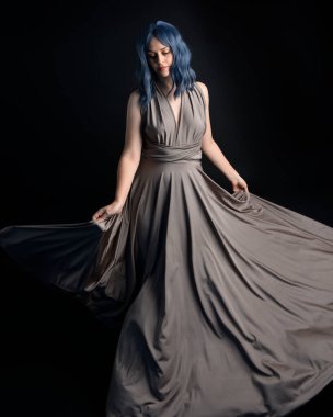 portrait of pretty girl with blue hair wig & elegant gown with expressive facial expressions & gestural arm poses. colourful neon gel lighting, isolated on studio background.