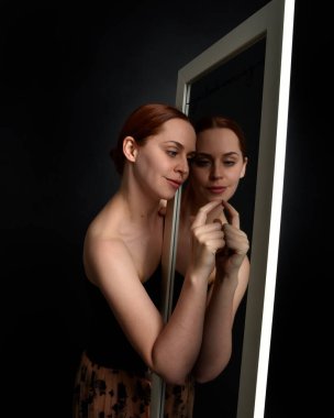 Close up portrait of beautiful girl looking into mirror, self reflection with colourful studio lighting.