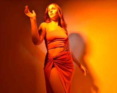 Low angle portrait of pretty girl wearing pink outfit, gestural arm poses reaching out as if casting a spell, colourful neon gel lighting, isolated on studio background.