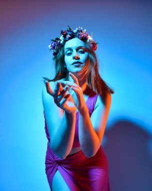 Low angle portrait of pretty girl wearing pink outfit, gestural arm poses reaching out as if casting a spell, colourful neon gel lighting, isolated on studio background.