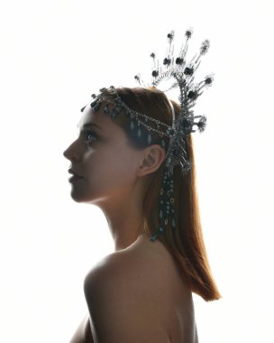 Close up portrait of beautiful girl in side profile, wearing an ornate silver crown headpiece, glowing silhouette lighting on white studio background.