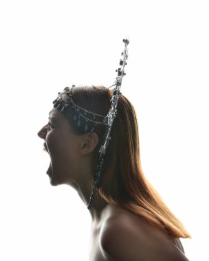 Close up portrait of beautiful girl in side profile, wearing an ornate silver crown headpiece, glowing silhouette lighting on white studio background.