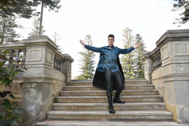 portrait of handsome brunette male model wearing fantasy medieval prince costume, romantic silk shirt. Wandering around historical castle location background with stone staircase.
