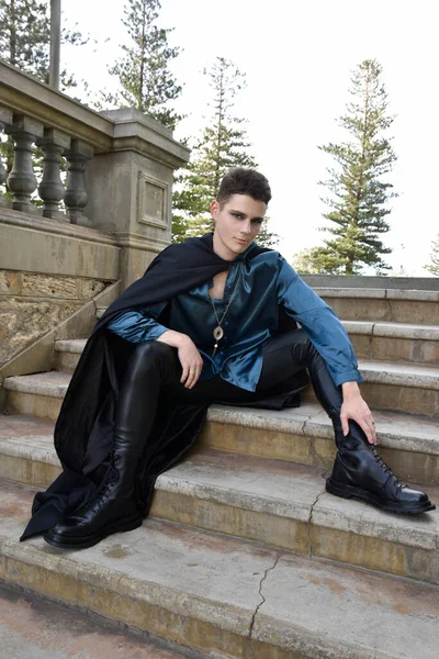 portrait of handsome brunette male model wearing fantasy medieval prince costume, romantic silk shirt. Wandering around historical castle location background with stone staircase.