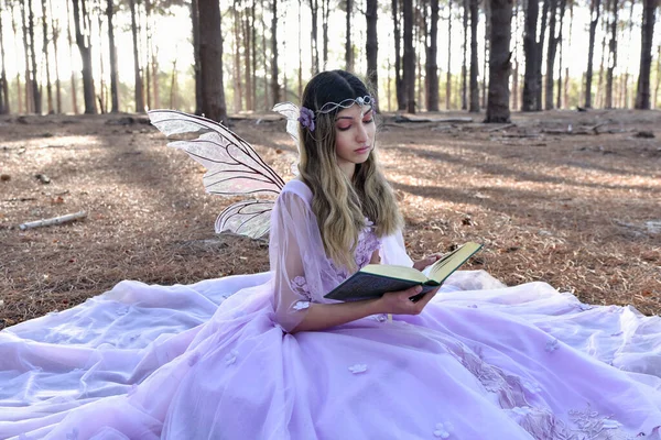 Fun length  portrait of beautiful young blonde model wearing a purple princess fantasy ball gown with flower crown diadem. Sitting pose in pine tree forest location background with golden lighting.